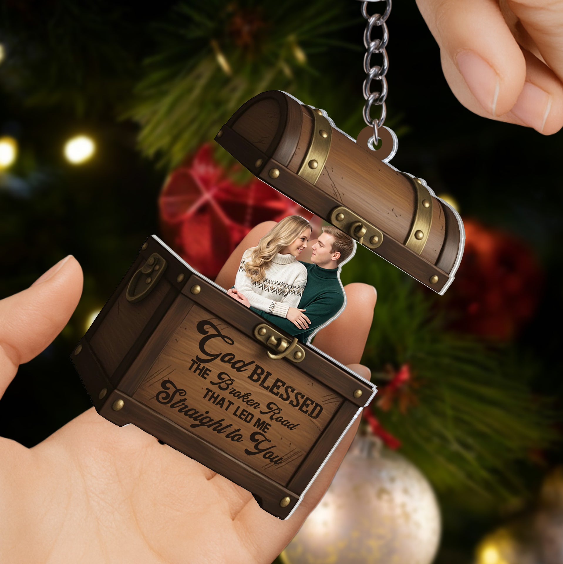 Personalized treasure chest sliding photo keychain held by a hand in front of a warm, blurry Christmas tree with holiday lights